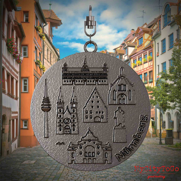 Halskette mit Drehwirbel und Vorderseite eines Schmuckanhängers aus Titan, auf dem Reliefs bekannter Sehenswürdigkeiten der Stadt Nuernberg abgebildet sind. Den Hintergrund bildet eine Ansicht der Stadt Nurenberg.