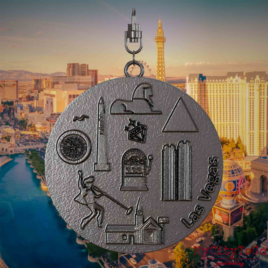 Halskette mit Drehwirbel und Vorderseite eines Schmuckanhängers aus Titan, auf dem Reliefs bekannter Sehenswürdigkeiten der Stadt Las Vegas  abgebildet sind. Den Hintergrund bildet eine Ansicht der Stadt Las Vegas.
