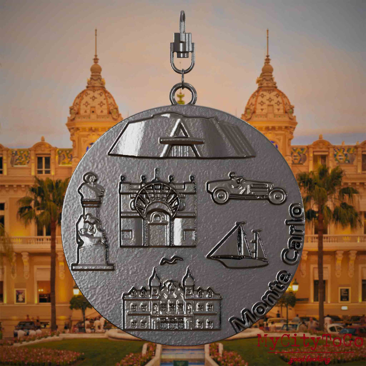 Halskette mit Drehwirbel und Vorderseite eines Schmuckanhängers aus Titan, auf dem Reliefs bekannter Sehenswürdigkeiten der Stadt Monte Carlo abgebildet sind. Den Hintergrund bildet eine Ansicht der Stadt Monte Carlo.
