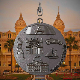 Halskette mit Drehwirbel und Vorderseite eines Schmuckanhängers aus Titan, auf dem Reliefs bekannter Sehenswürdigkeiten der Stadt Monte Carlo abgebildet sind. Den Hintergrund bildet eine Ansicht der Stadt Monte Carlo.
