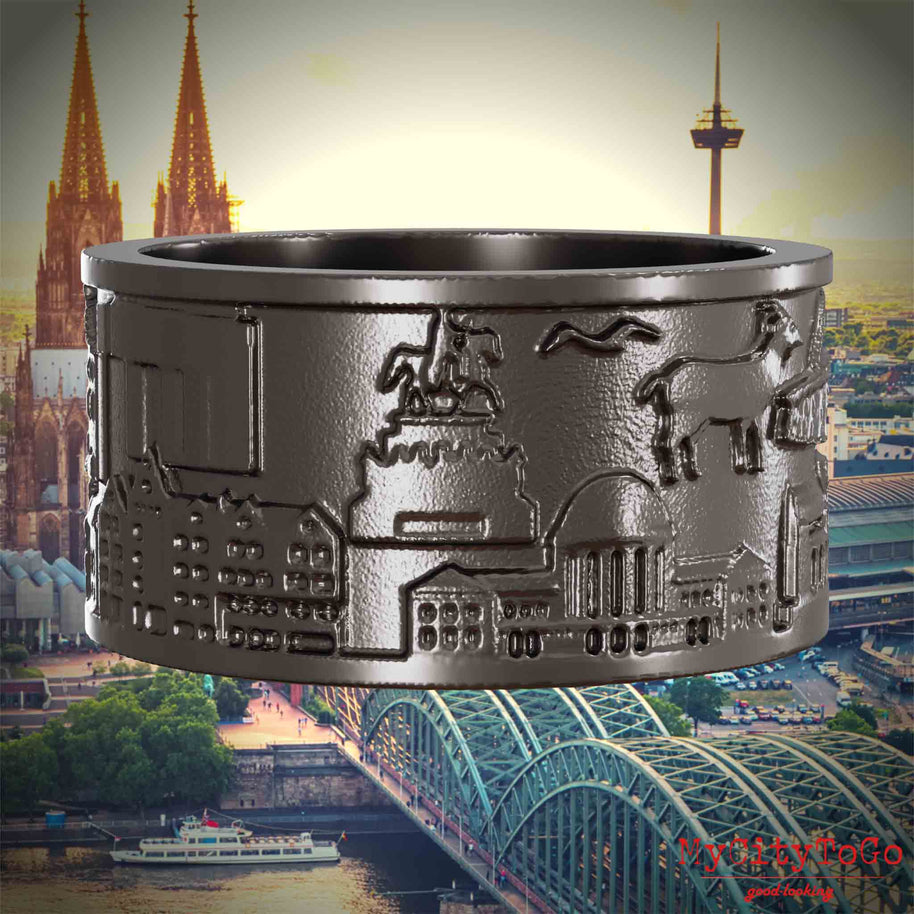 Ring aus Titan mit Reliefs bekannter Sehenswürdigkeiten der Stadt Koeln. Den Hintergrund bildet eine Ansicht der Stadt Koeln.