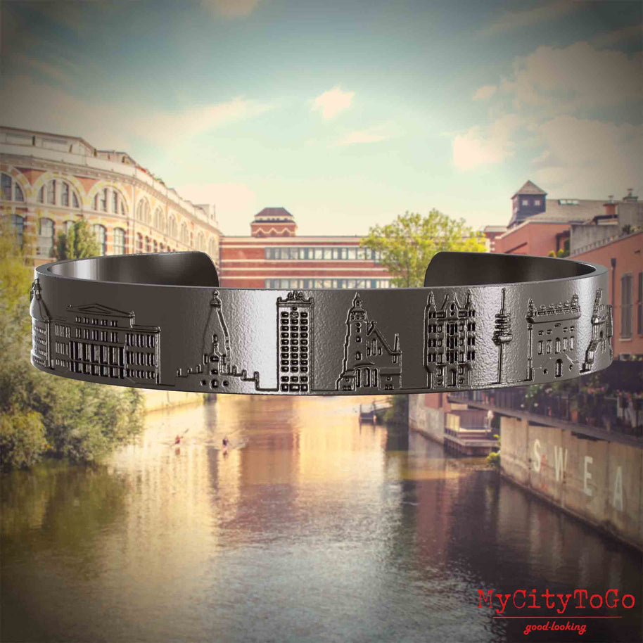 Armreif aus Titan mit Reliefs bekannter Sehenswürdigkeiten der Stad Leipzig. Den Hintergrund bildet eine Ansicht der Stadt Leipzig.