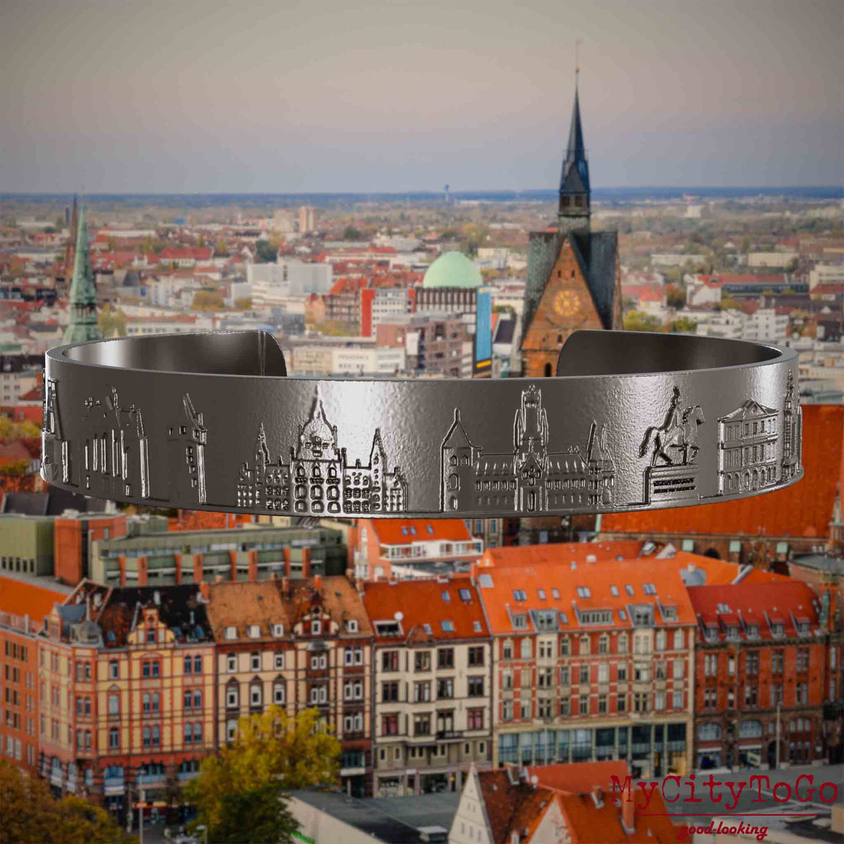 Armreif aus Titan mit Reliefs bekannter Sehenswürdigkeiten der Stadt Hannover. Den Hintergrund bildet eine Ansicht der Stadt Hannover.