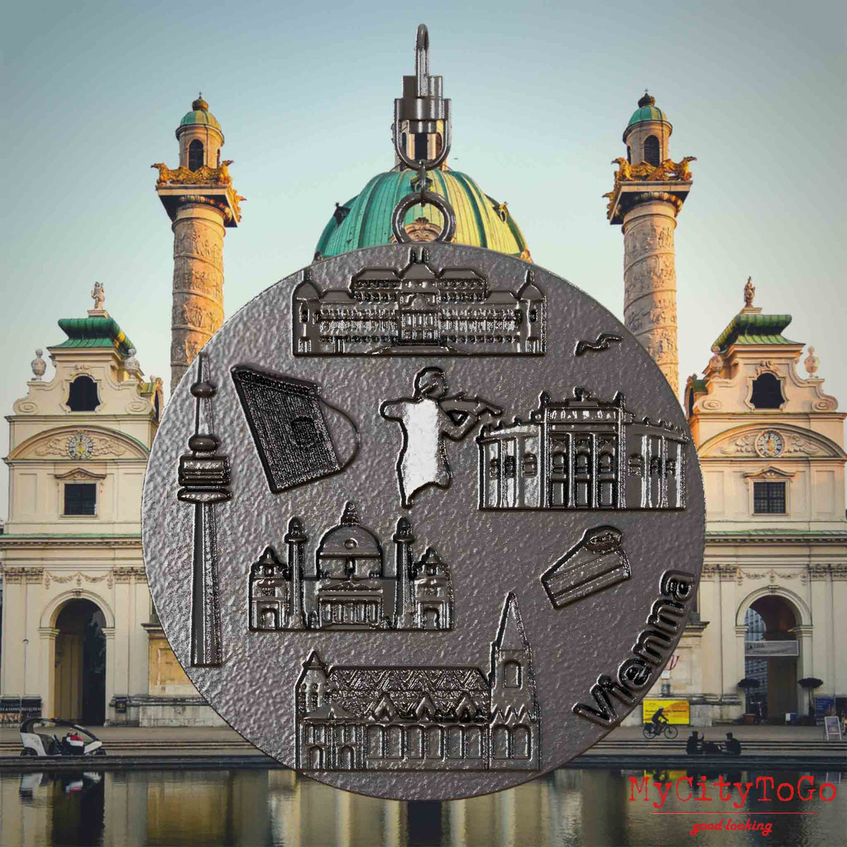 Halskette mit Drehwirbel und Rückseite eines Schmuckanhängers aus Titan, auf dem Reliefs bekannter Sehenswürdigkeiten der Stadt Wien abgebildet sind. Den Hintergrund bildet eine Ansicht der Stadt Wien.
