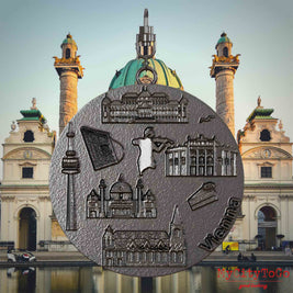 Halskette mit Drehwirbel und Rückseite eines Schmuckanhängers aus Titan, auf dem Reliefs bekannter Sehenswürdigkeiten der Stadt Wien abgebildet sind. Den Hintergrund bildet eine Ansicht der Stadt Wien.
