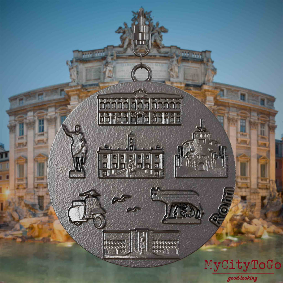Halskette mit Drehwirbel und Vorderseite eines Schmuckanhängers aus Titan, auf dem Reliefs bekannter Sehenswürdigkeiten der Stadt Rom abgebildet sind. Den Hintergrund bildet eine Ansicht der Stadt Rom.
