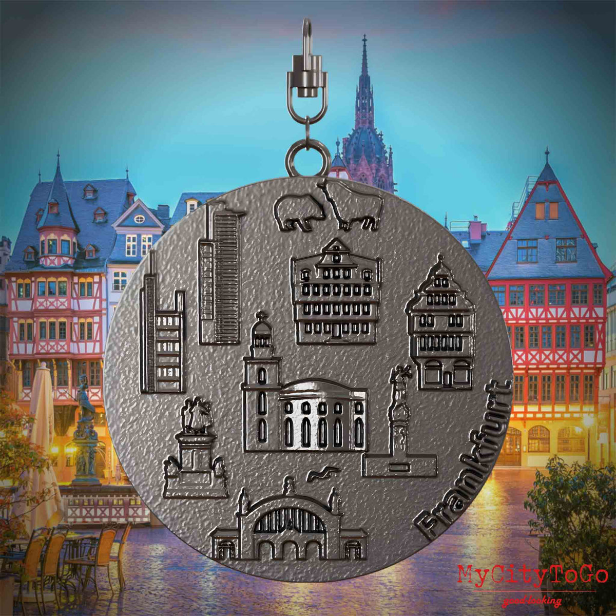 Halskette mit Drehwirbel und Vorderseite eines Schmuckanhängers aus Titan, auf dem Reliefs bekannter Sehenswürdigkeiten der Stadt Frankfurt abgebildet sind. Den Hintergrund bildet eine Ansicht der Stadt Frankfurt.