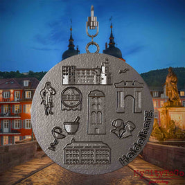 Halskette mit Drehwirbel und Vorderseite eines Schmuckanhängers aus Titan, auf dem Reliefs bekannter Sehenswürdigkeiten der Stadt Heidelberg abgebildet sind. Den Hintergrund bildet eine Ansicht der Stadt Heidelberg .
