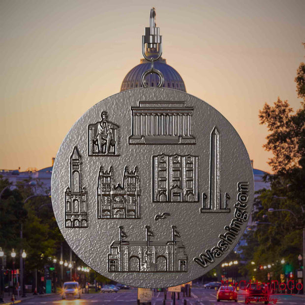 Halskette mit Drehwirbel und Vorderseite eines Schmuckanhängers aus Titan, auf dem Reliefs bekannter Sehenswürdigkeiten der Stadt Washington abgebildet sind. Den Hintergrund bildet eine Ansicht der Stadt Washington.
