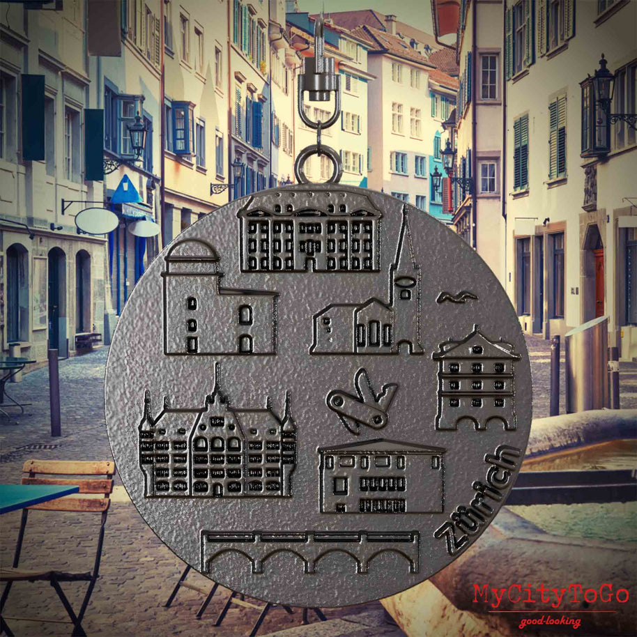 Halskette mit Drehwirbel und Rückseite eines Schmuckanhängers aus Titan, auf dem Reliefs bekannter Sehenswürdigkeiten der Stadt Zuerich abgebildet sind. Den Hintergrund bildet eine Ansicht der Stadt Zuerich.
