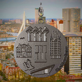 Halskette mit Drehwirbel und Vorderseite eines Schmuckanhängers aus Titan, auf dem Reliefs bekannter Sehenswürdigkeiten der Stadt Rotterdam abgebildet sind. Den Hintergrund bildet eine Ansicht der Stadt Rotterdam.
