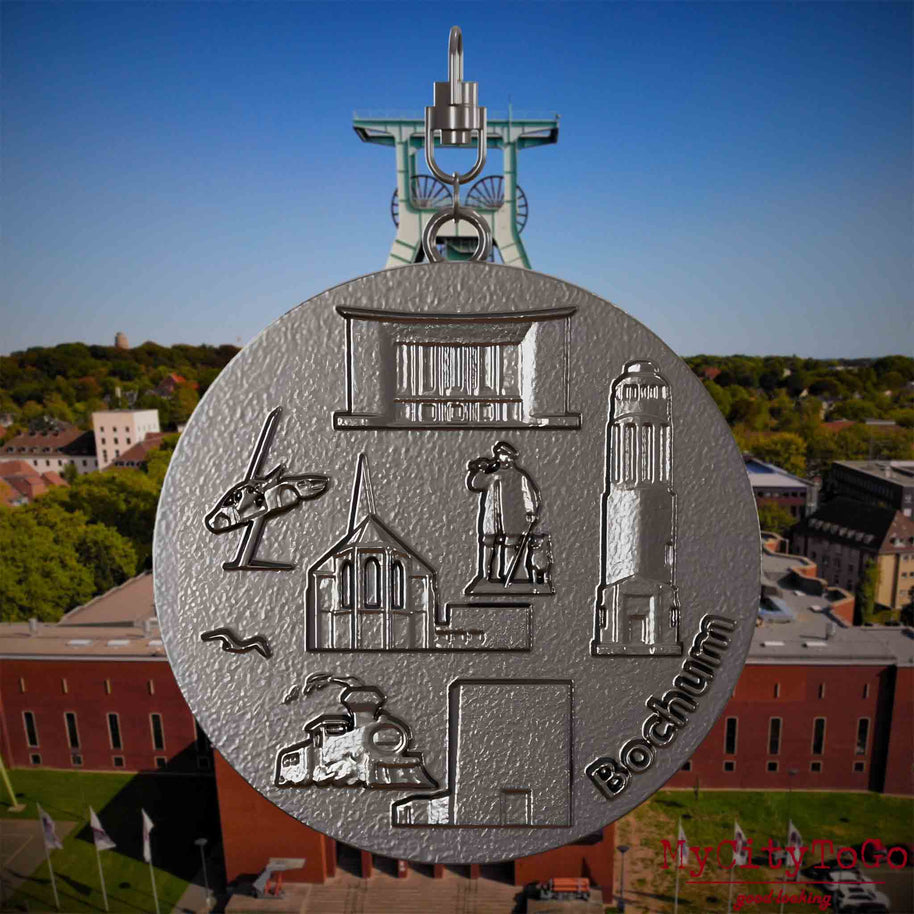 Halskette mit Drehwirbel und Rückseite eines Schmuckanhängers aus Titan, auf dem Reliefs bekannter Sehenswürdigkeiten der Stadt Bochum abgebildet sind. Den Hintergrund bildet eine Ansicht der Stadt Bochum .
