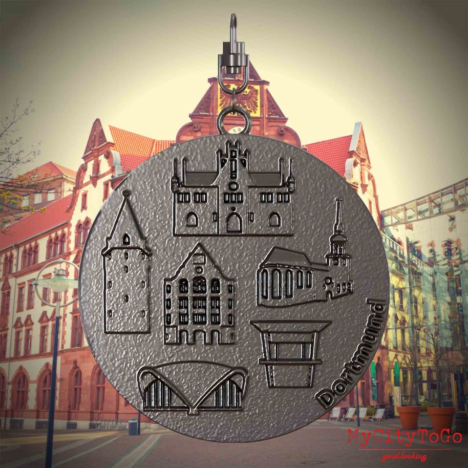 Halskette mit Drehwirbel und Rückseite eines Schmuckanhängers aus Titan, auf dem Reliefs bekannter Sehenswürdigkeiten der Stadt Dortmund abgebildet sind. Den Hintergrund bildet eine Ansicht der Stadt Dortmund.