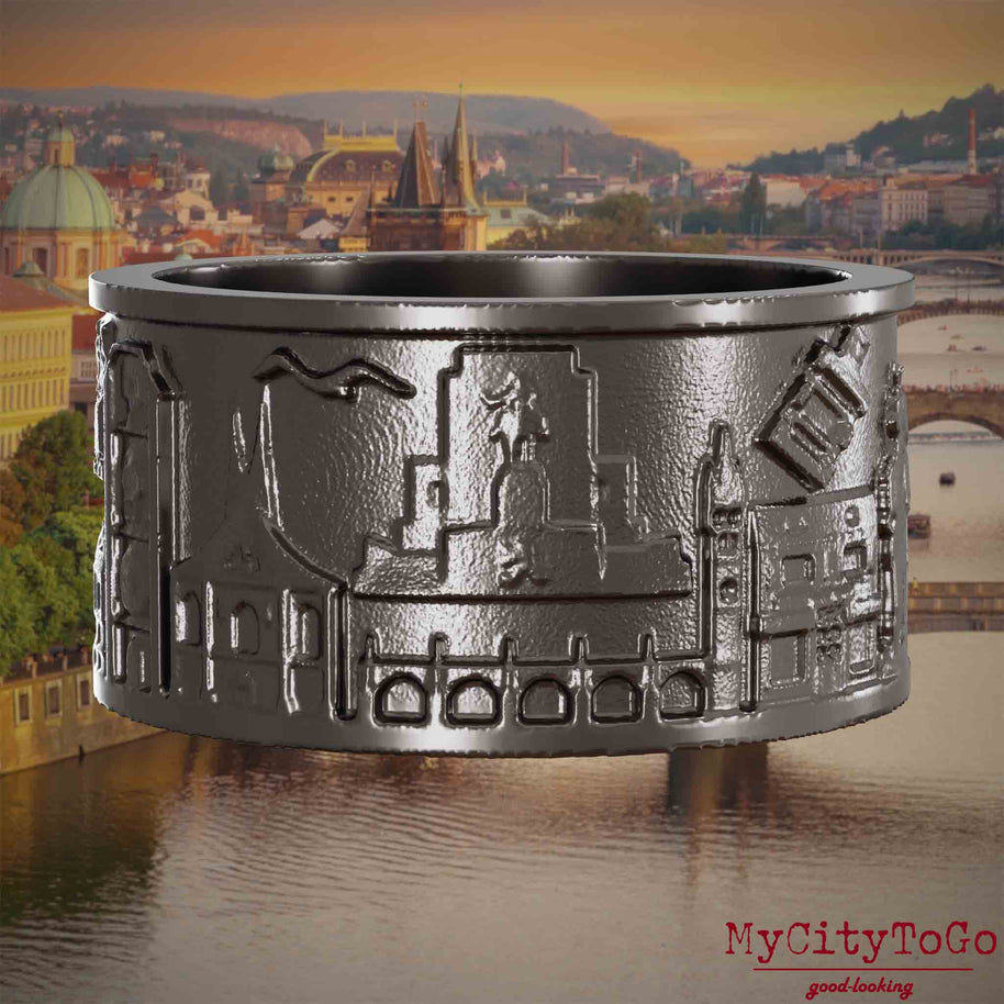 Ring aus Titan mit Reliefs bekannter Sehenswürdigkeiten der Stadt Prag. Den Hintergrund bildet eine Ansicht der Stadt Prag.