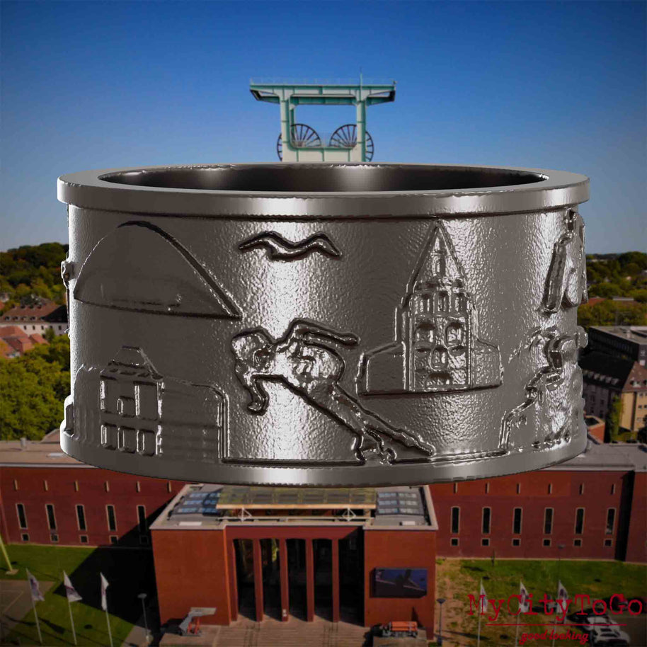Ring aus Titan mit Reliefs bekannter Sehenswürdigkeiten der Stadt Bochum. Den Hintergrund bildet eine Ansicht der Stadt Bochum.