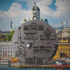 Halskette mit Drehwirbel und Vorderseite eines Schmuckanhängers aus Titan, auf dem Reliefs bekannter Sehenswürdigkeiten der Stadt Helsinki abgebildet sind. Den Hintergrund bildet eine Ansicht der Stadt Helsinki.
