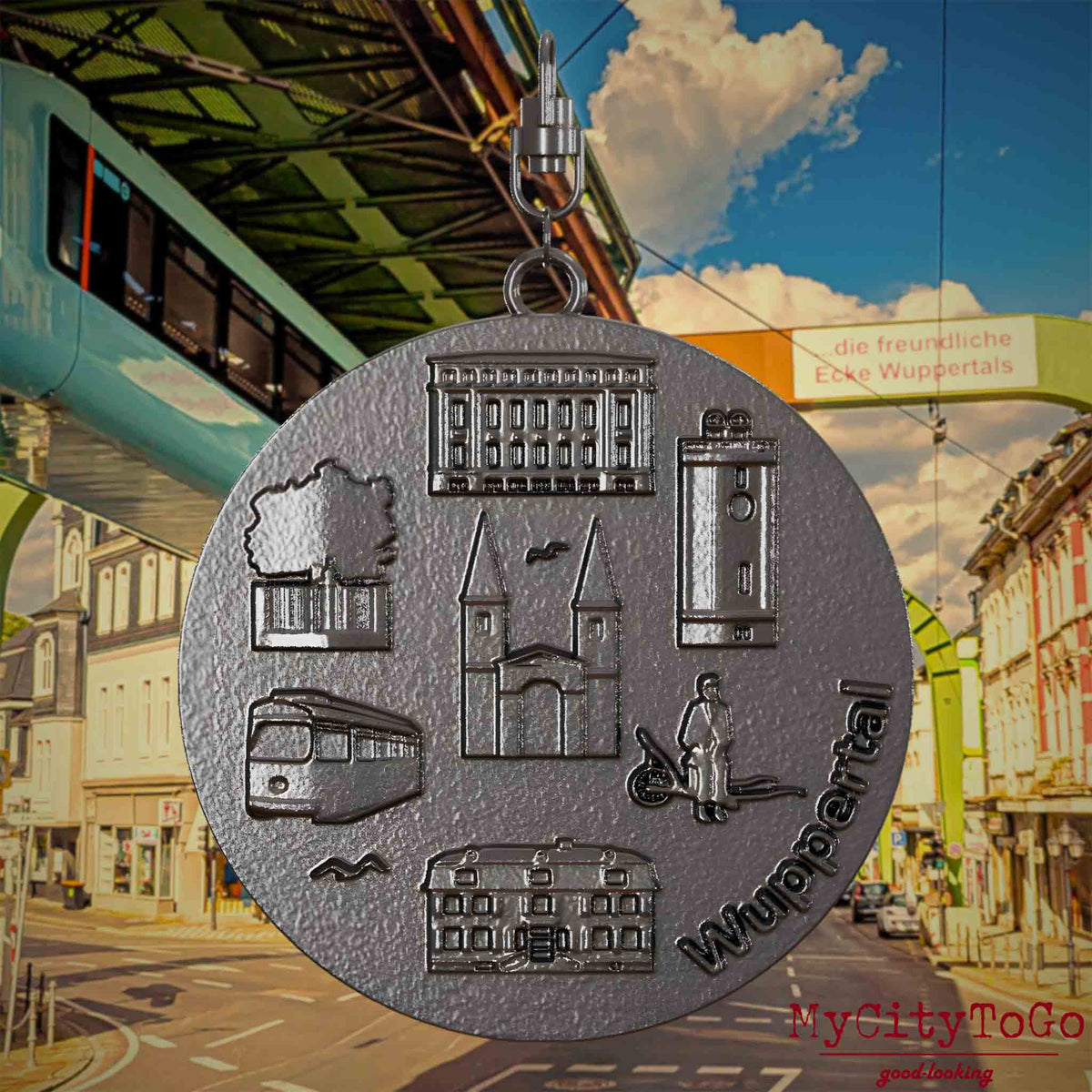 Halskette mit Drehwirbel und Rückseite eines Schmuckanhängers aus Titan, auf dem Reliefs bekannter Sehenswürdigkeiten der Stadt Wuppertal abgebildet sind. Den Hintergrund bildet eine Ansicht der Stadt Wuppertal.
