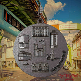 Halskette mit Drehwirbel und Rückseite eines Schmuckanhängers aus Titan, auf dem Reliefs bekannter Sehenswürdigkeiten der Stadt Wuppertal abgebildet sind. Den Hintergrund bildet eine Ansicht der Stadt Wuppertal.
