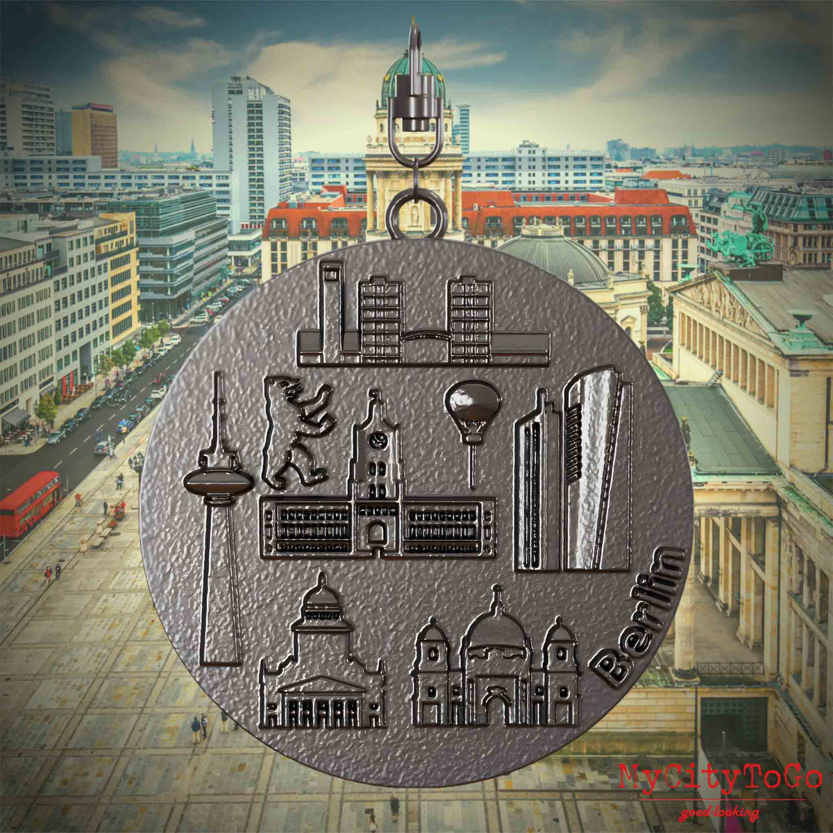 Halskette mit Drehwirbel und Vorderseite eines Schmuckanhängers aus Titan, auf dem Reliefs bekannter Sehenswürdigkeiten der Stadt Berlin abgebildet sind. Den Hintergrund bildet eine Ansicht der Stadt Berlin.