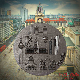Halskette mit Drehwirbel und Vorderseite eines Schmuckanhängers aus Titan, auf dem Reliefs bekannter Sehenswürdigkeiten der Stadt Berlin abgebildet sind. Den Hintergrund bildet eine Ansicht der Stadt Berlin.