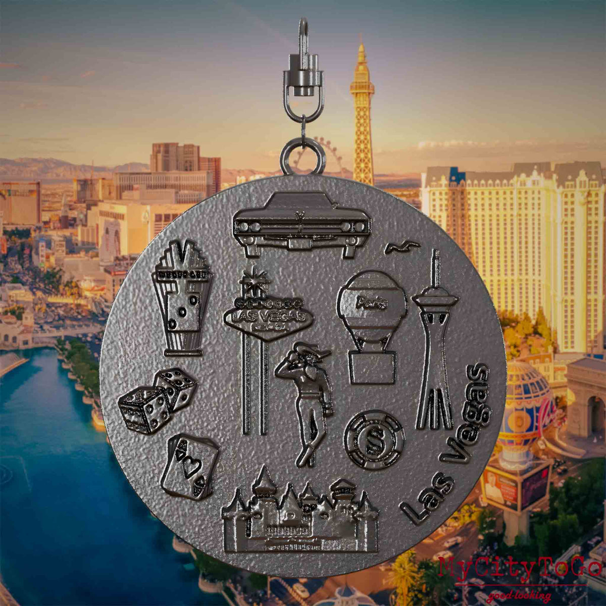 Halskette mit Drehwirbel und Rückseite eines Schmuckanhängers aus Titan, auf dem Reliefs bekannter Sehenswürdigkeiten der Stadt Las Vegas abgebildet sind. Den Hintergrund bildet eine Ansicht der Stadt Las Vegas.
