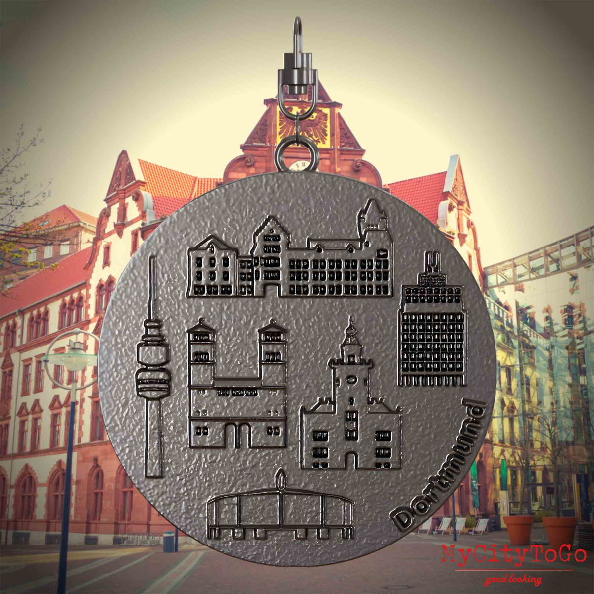 Halskette mit Drehwirbel und Vorderseite eines Schmuckanhängers aus Titan, auf dem Reliefs bekannter Sehenswürdigkeiten der Stadt Dortmund abgebildet sind. Den Hintergrund bildet eine Ansicht der Stadt Dortmund.