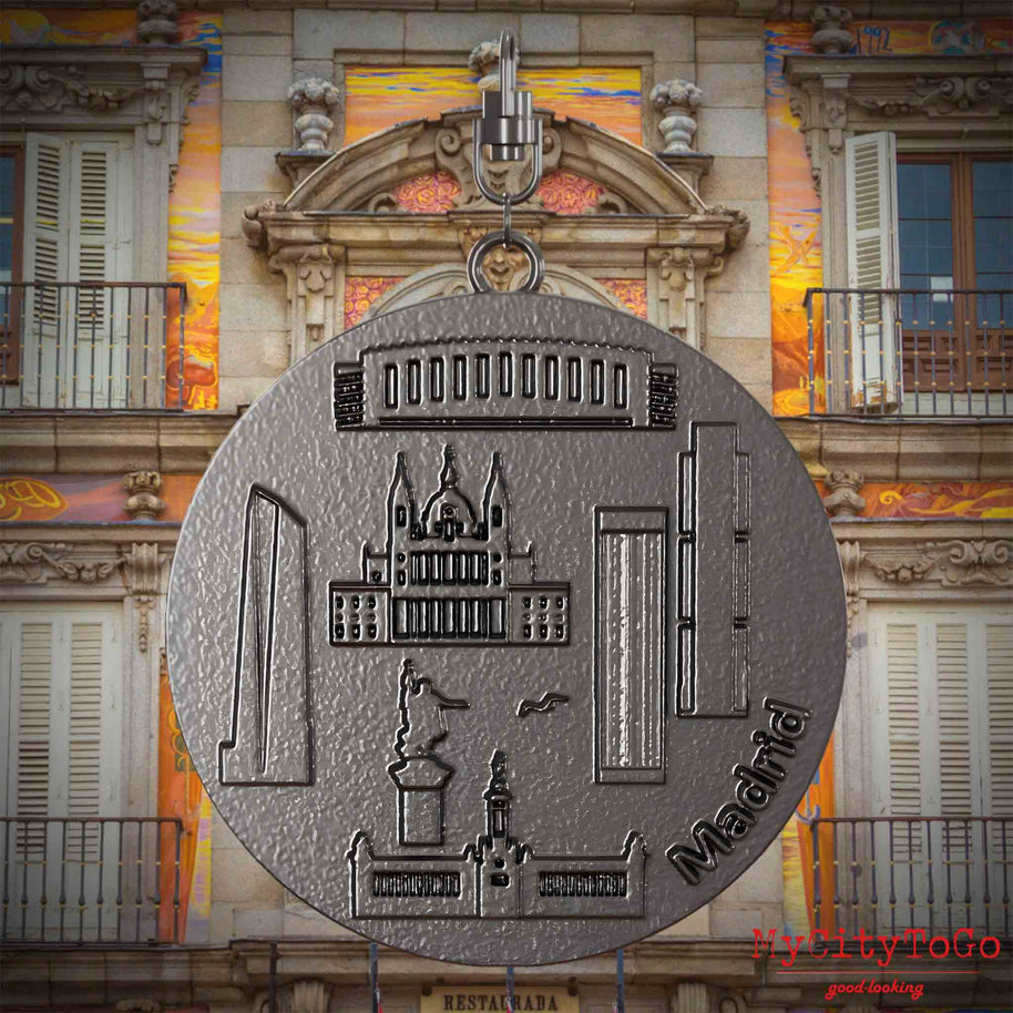 Halskette mit Drehwirbel und Rückseite eines Schmuckanhängers aus Titan, auf dem Reliefs bekannter Sehenswürdigkeiten der Stadt Madrid abgebildet sind. Den Hintergrund bildet eine Ansicht der Stadt Madrid.
