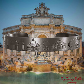 Armreif aus Titan mit Reliefs bekannter Sehenswürdigkeiten der Stadt Rom. Den Hintergrund bildet eine Ansicht der Stadt Rom.