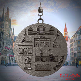Halskette mit Drehwirbel und Rückseite eines Schmuckanhängers aus Titan, auf dem Reliefs bekannter Sehenswürdigkeiten der Stadt Muenchen abgebildet sind. Den Hintergrund bildet eine Ansicht der Stadt Muenchen.