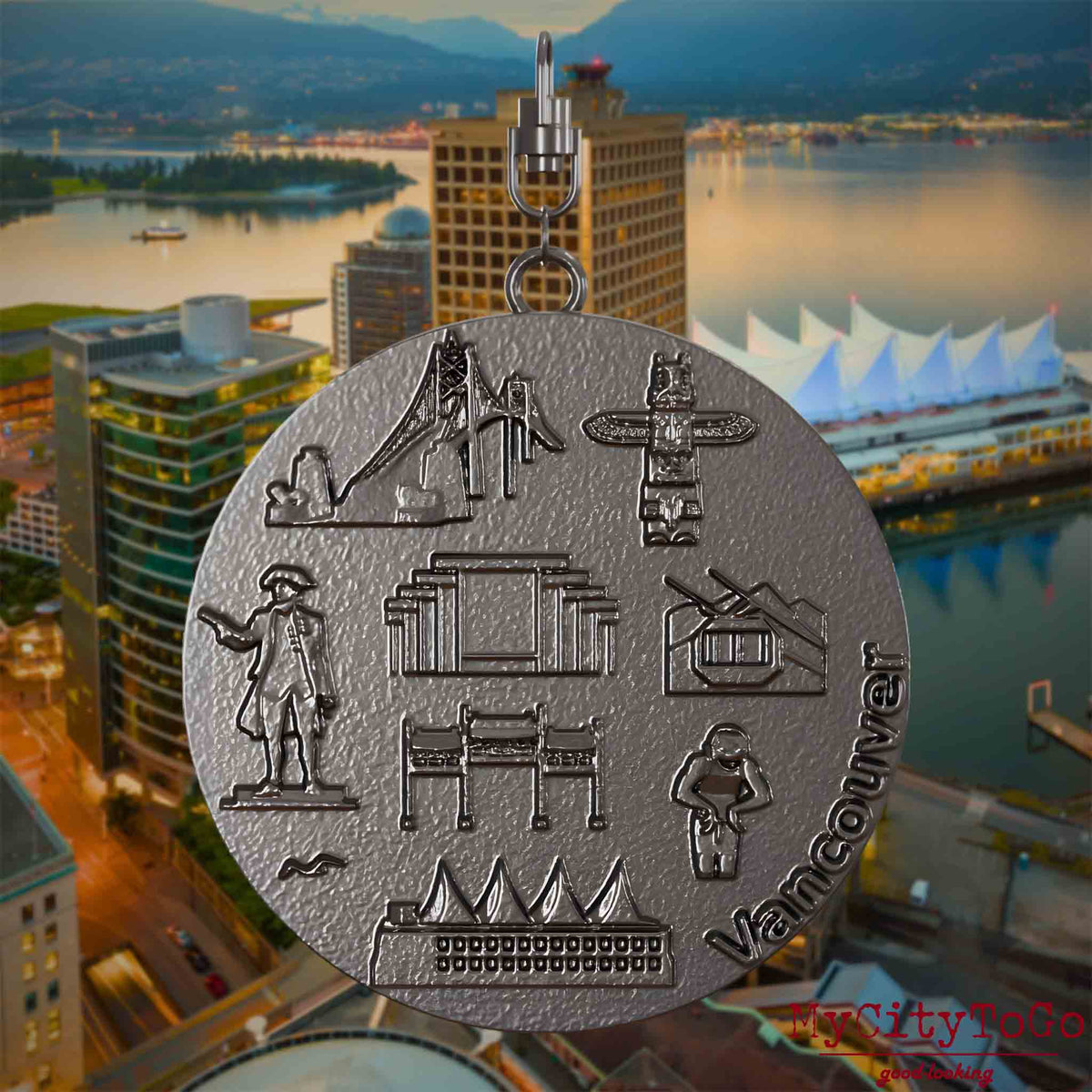 Halskette mit Drehwirbel und Vorderseite eines Schmuckanhängers aus Titan, auf dem Reliefs bekannter Sehenswürdigkeiten der Stadt Vancouver abgebildet sind. Den Hintergrund bildet eine Ansicht der Stadt Vancouver.
