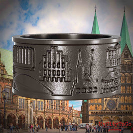 Ring aus Titan mit Reliefs bekannter Sehenswürdigkeiten der Stadt Bremen. Den Hintergrund bildet eine Ansicht der Stadt Bremen.