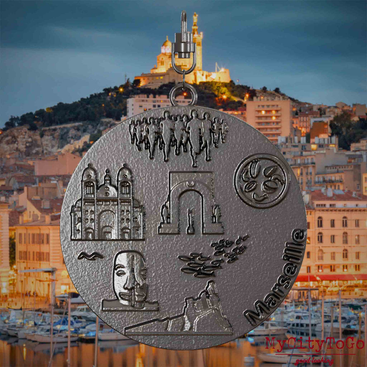 Halskette mit Drehwirbel und Rückseite eines Schmuckanhängers aus Titan, auf dem Reliefs bekannter Sehenswürdigkeiten der Stadt Marseille abgebildet sind. Den Hintergrund bildet eine Ansicht der Stadt Marseille.
