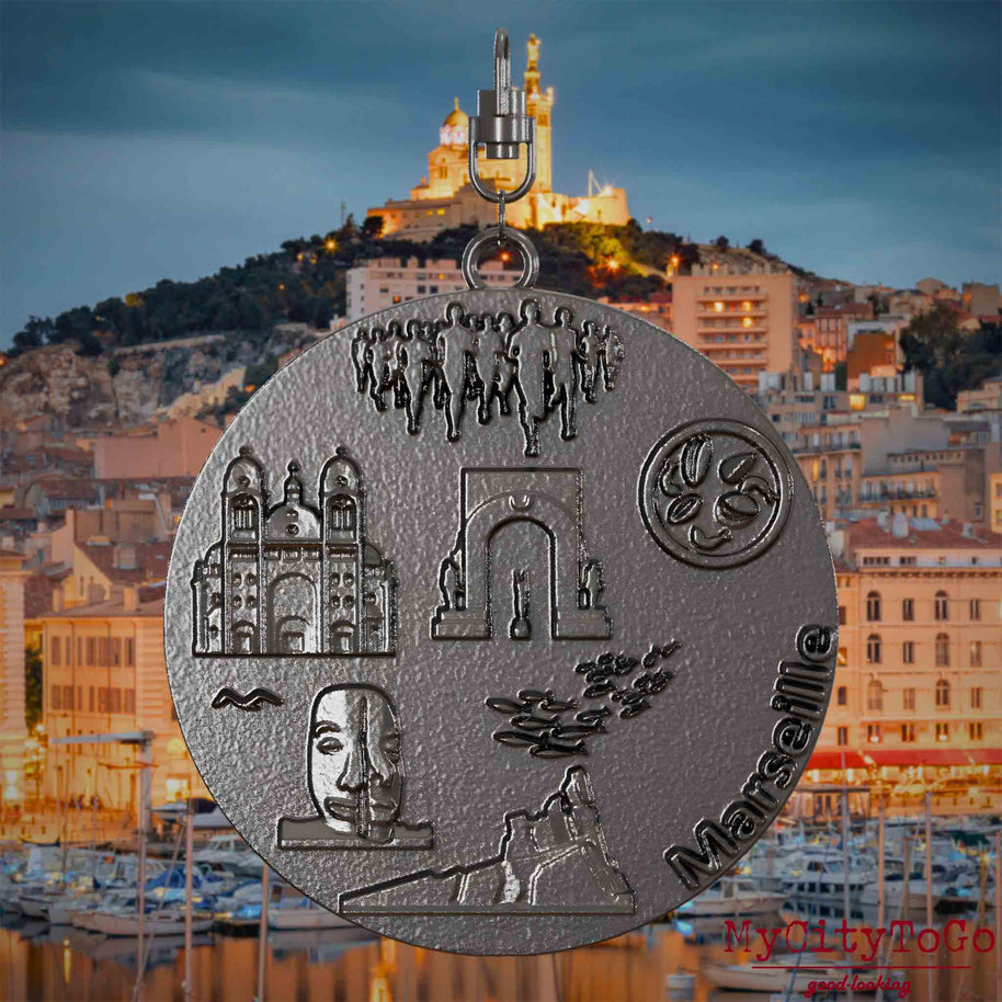Halskette mit Drehwirbel und Rückseite eines Schmuckanhängers aus Titan, auf dem Reliefs bekannter Sehenswürdigkeiten der Stadt Marseille abgebildet sind. Den Hintergrund bildet eine Ansicht der Stadt Marseille.
