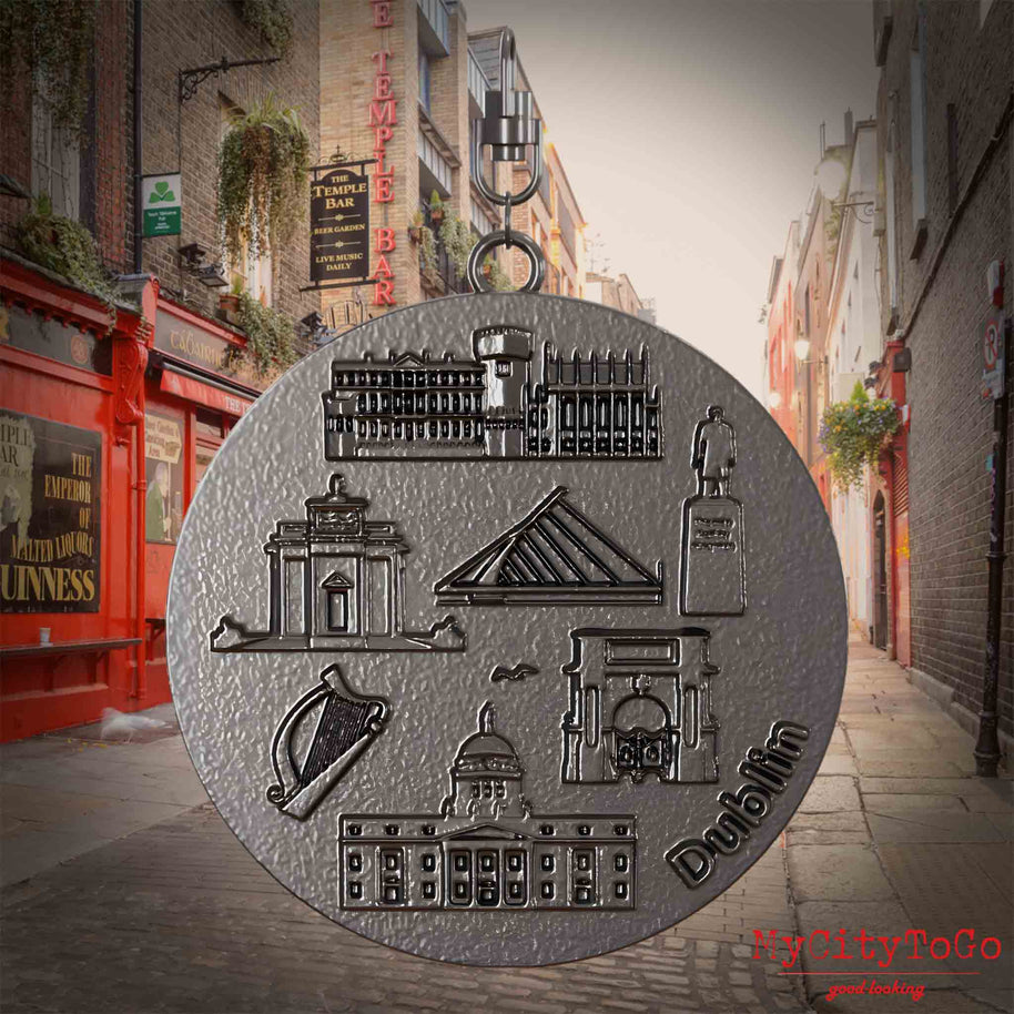 Halskette mit Drehwirbel und Rückseite eines Schmuckanhängers aus Titan, auf dem Reliefs bekannter Sehenswürdigkeiten der Stadt Dublin abgebildet sind. Den Hintergrund bildet eine Ansicht der Stadt Dublin.
