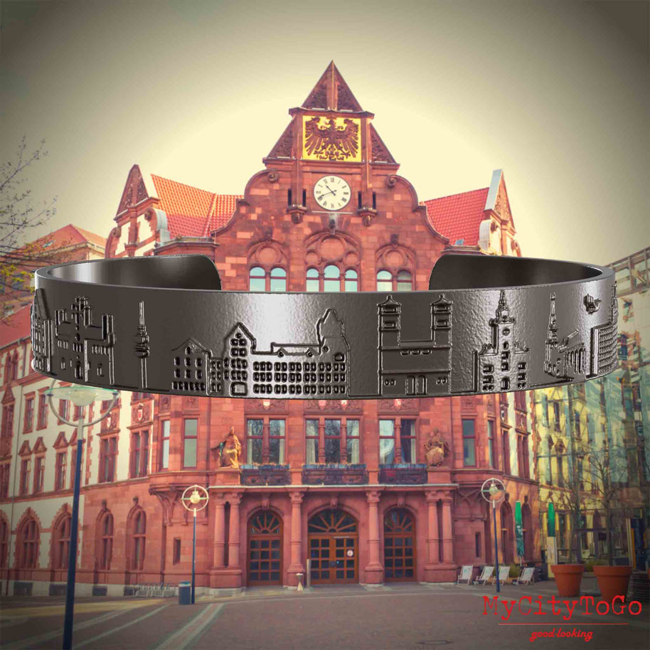 Armreif aus Titan mit Reliefs bekannter Sehenswürdigkeiten der Stadt Dortmund. Den Hintergrund bildet eine Ansicht der Stadt Dortmund.