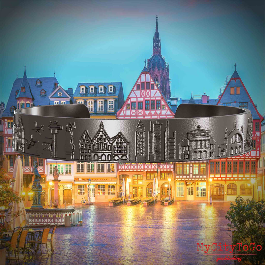 Armreif aus Titan mit Reliefs bekannter Sehenswürdigkeiten der Stadt Frankfurt. Den Hintergrund bildet eine Ansicht der Stadt Frankfurt.