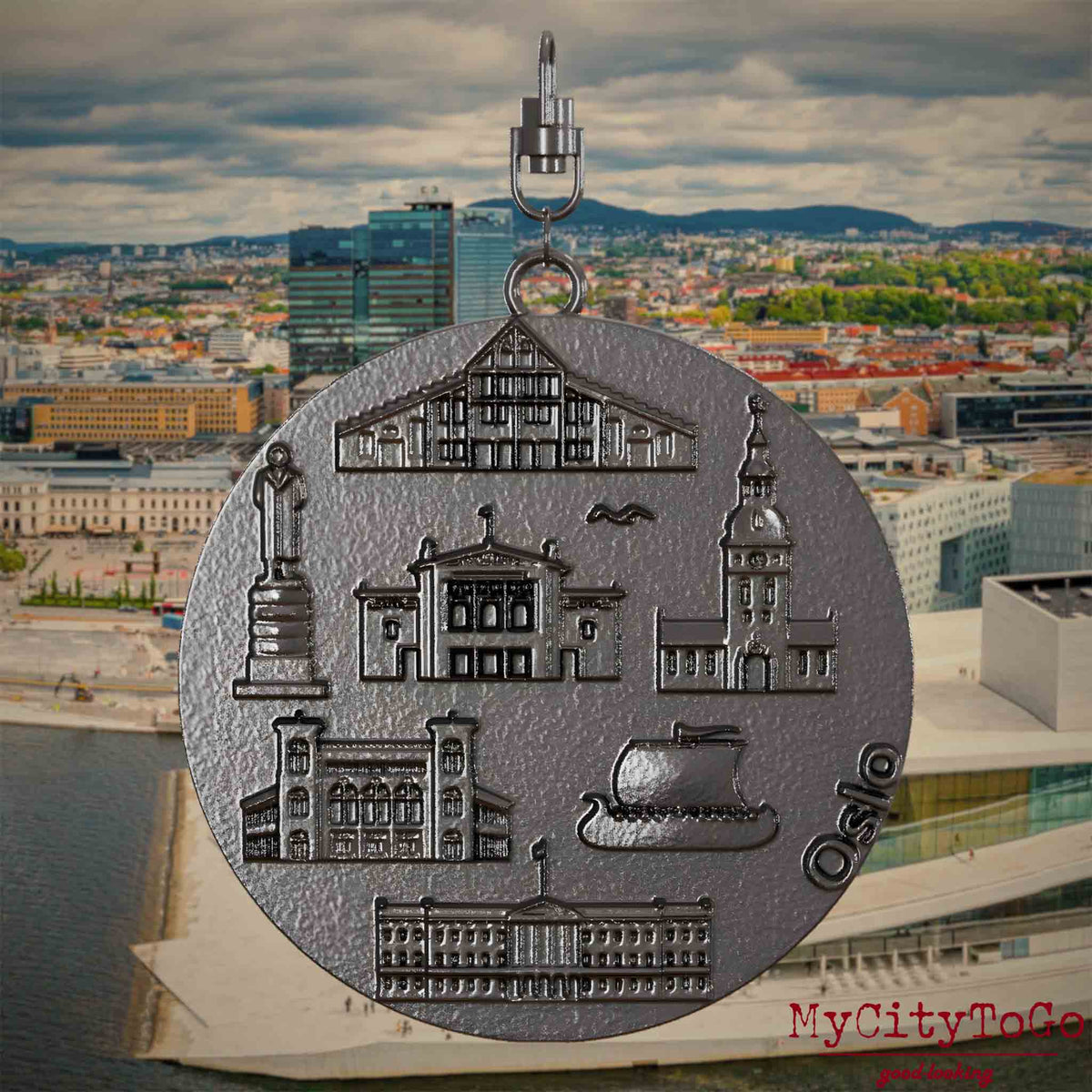Halskette mit Drehwirbel und Rückseite eines Schmuckanhängers aus Titan, auf dem Reliefs bekannter Sehenswürdigkeiten der Stadt Oslo abgebildet sind. Den Hintergrund bildet eine Ansicht der Stadt Oslo.
