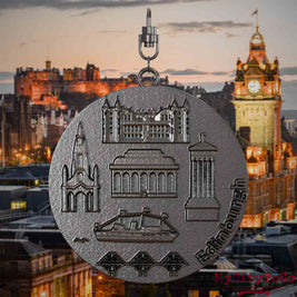 Halskette mit Drehwirbel und Rückseite eines Schmuckanhängers aus Titan, auf dem Reliefs bekannter Sehenswürdigkeiten der Stadt Edinburgh abgebildet sind. Den Hintergrund bildet eine Ansicht der Stadt Edinburgh.
