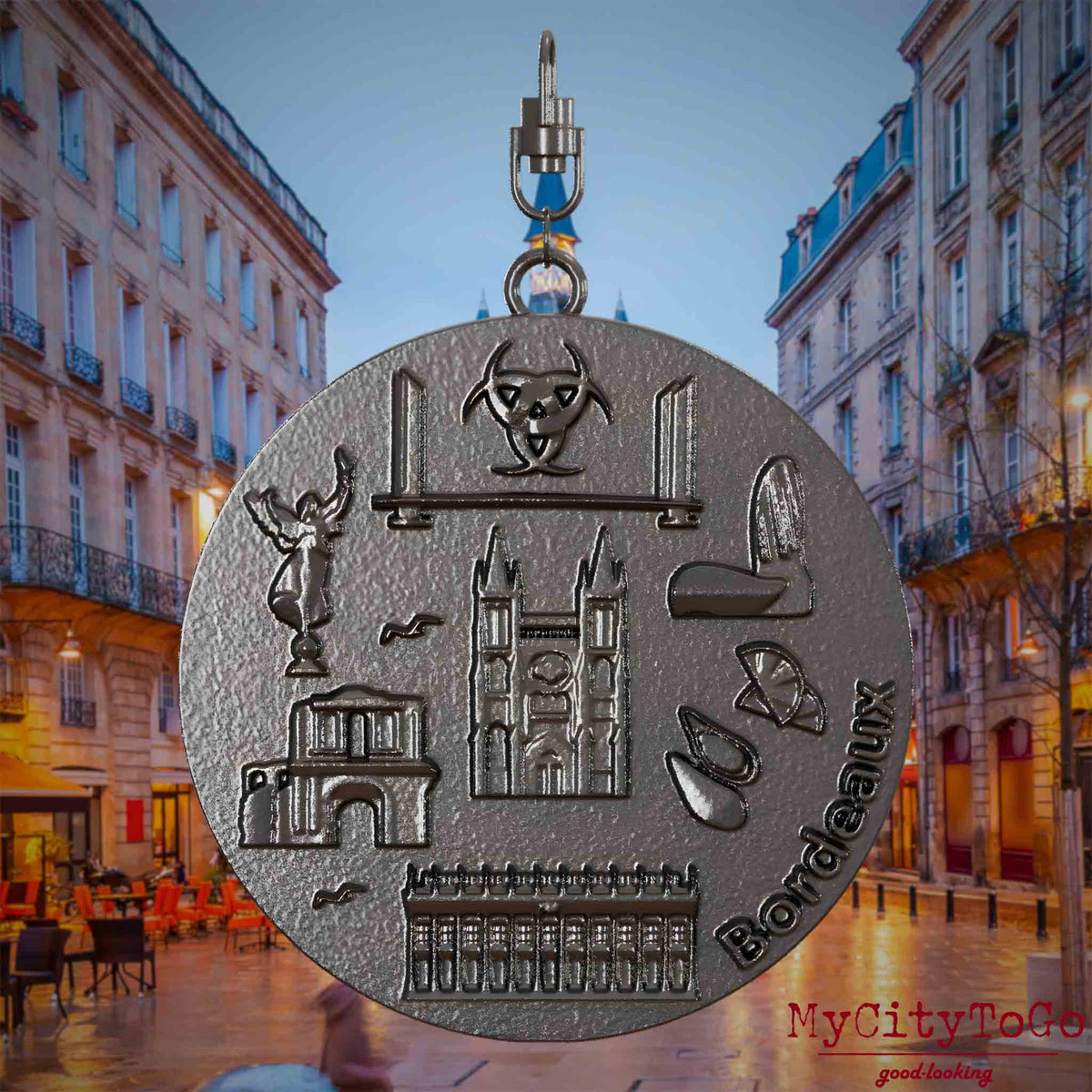 Halskette mit Drehwirbel und Vorderseite eines Schmuckanhängers aus Titan, auf dem Reliefs bekannter Sehenswürdigkeiten der Stadt Bordeaux abgebildet sind. Den Hintergrund bildet eine Ansicht der Stadt Bordeaux.
