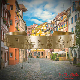 Armreif aus vergoldetem Edelstahl mit Reliefs bekannter Sehenswürdigkeiten der Stadt Nürnberg. Den Hintergrund bildet eine Ansicht der Stadt  Nuernberg.