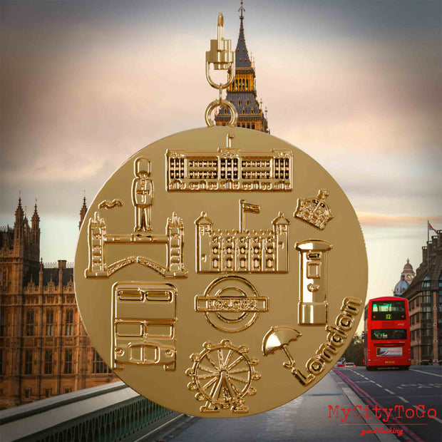 Halskette mit Drehwirbel und Vorderseite eines vergoldeten Schmuckanhängers, auf dem Reliefs bekannter Sehenswürdigkeiten der Stadt London abgebildet sind. Den Hintergrund bildet eine Ansicht der Stadt London.
