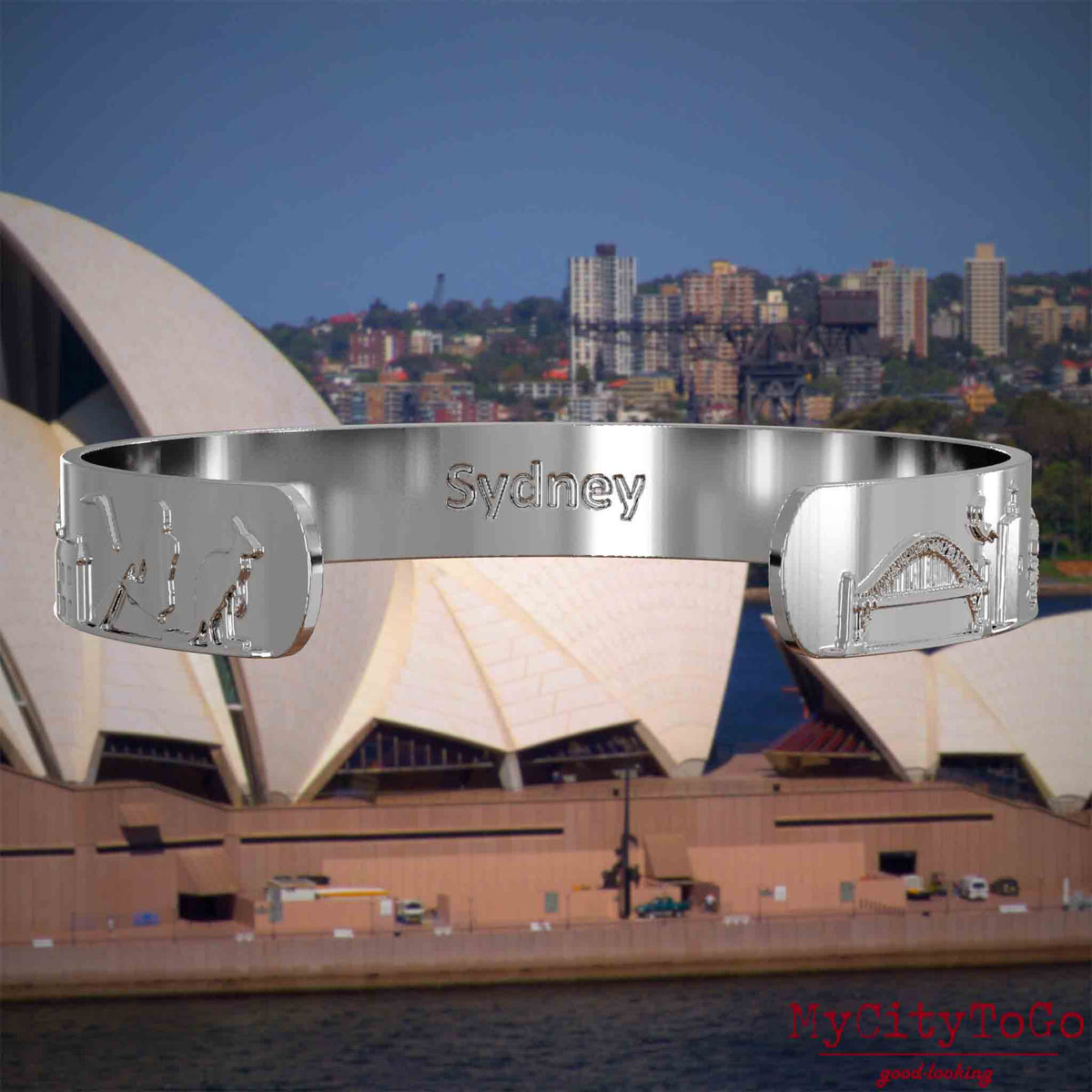 Innenseite eines silbernen Armreifs mit Reliefs bekannter Sehenswürdigkeiten der Stadt Sydney und einer Gravur des Stadtnamens . Den Hintergrund bildet eine Ansicht der Stadt Sydney.