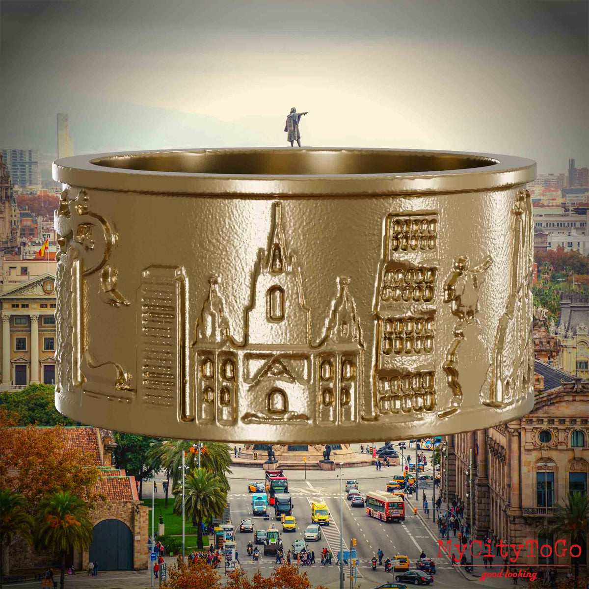 Ring aus vergoldetem Edelstahl mit Reliefs bekannter Sehenswürdigkeiten der Stadt Barcelona. Den Hintergrund bildet eine Ansicht der Stadt Barcelona.