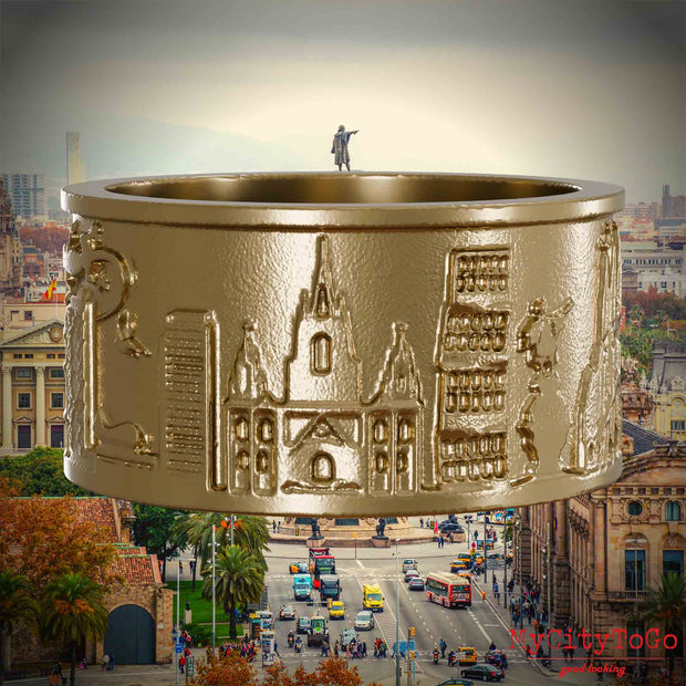 Ring aus vergoldetem Edelstahl mit Reliefs bekannter Sehenswürdigkeiten der Stadt Barcelona. Den Hintergrund bildet eine Ansicht der Stadt Barcelona.