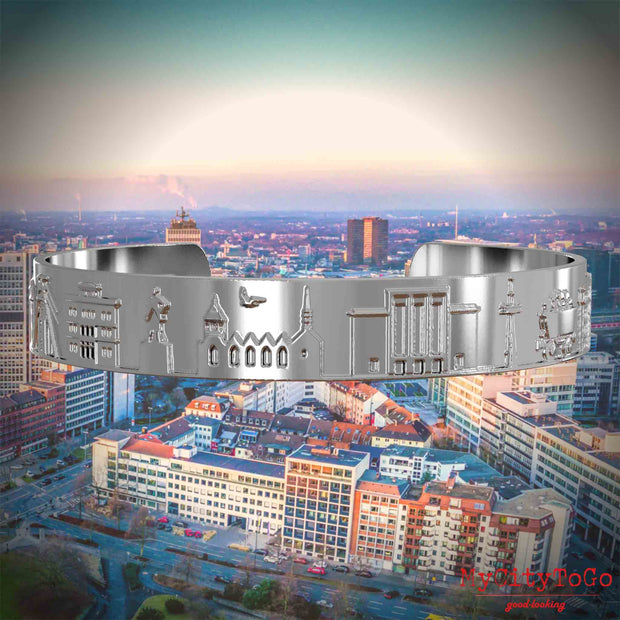 Versilberter Armreif mit Reliefs bekannter Sehenswürdigkeiten der Stadt Essen. Den Hintergrund bildet eine Ansicht der Stadt Essen.