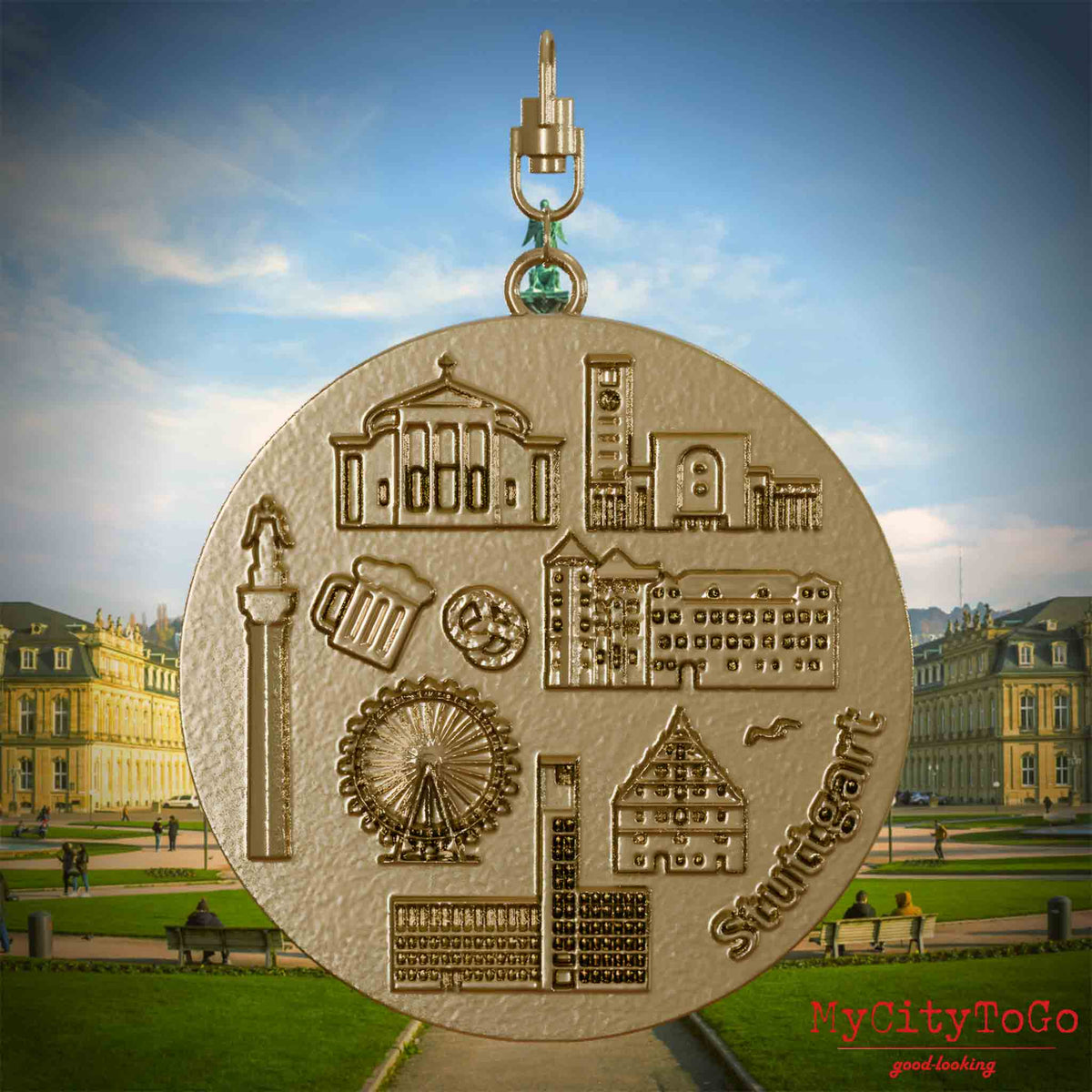Halskette mit Drehwirbel und Rückseite eines Schmuckanhängers aus vergoldetem Edelstahl, auf dem Reliefs bekannter Sehenswürdigkeiten der Stadt Stuttgart abgebildet sind. Den Hintergrund bildet eine Ansicht der Stadt Stuttgart.
