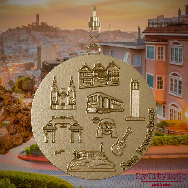 Halskette mit Drehwirbel und Rückseite eines Schmuckanhängers aus vergoldetem Edelstahl, auf dem Reliefs bekannter Sehenswürdigkeiten der Stadt San Francisco abgebildet sind. Den Hintergrund bildet eine Ansicht der Stadt San Francisco.
