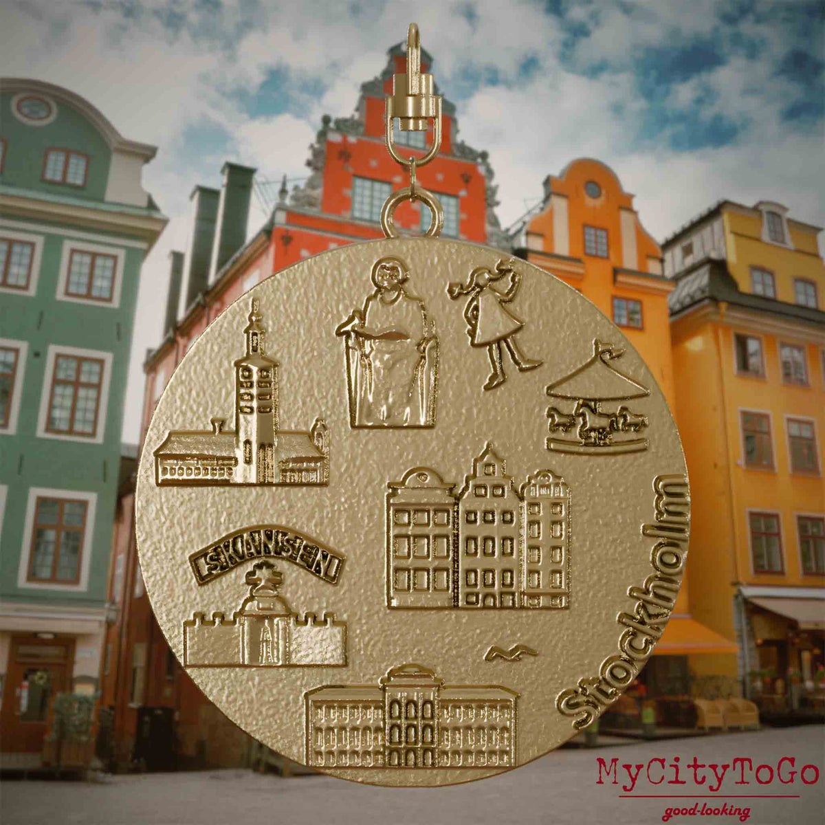 Halskette mit Drehwirbel und Rückseite eines Schmuckanhängers aus vergoldetem Edelstahl, auf dem Reliefs bekannter Sehenswürdigkeiten der Stadt Stockholm abgebildet sind. Den Hintergrund bildet eine Ansicht der Stadt Stockholm.
