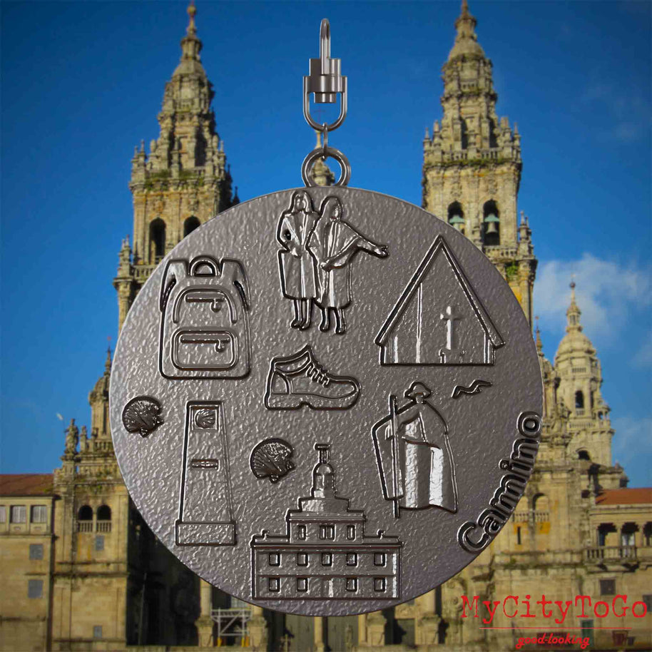 Halskette mit Drehwirbel und Vorderseite eines Schmuckanhängers aus Titan, auf dem Reliefs bekannter Sehenswürdigkeiten des Jakobswegs abgebildet sind. Den Hintergrund bildet eine Ansicht der Stadt Santiago de Compostela.
