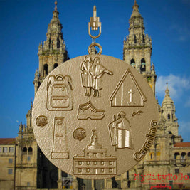 Halskette mit Drehwirbel und Rückseite eines Schmuckanhängers aus vergoldetem Edelstahl, auf dem Reliefs bekannter Sehenswürdigkeiten des Jakobswegs abgebildet sind. Den Hintergrund bildet eine Ansicht der Stadt Santiago de Compostela.